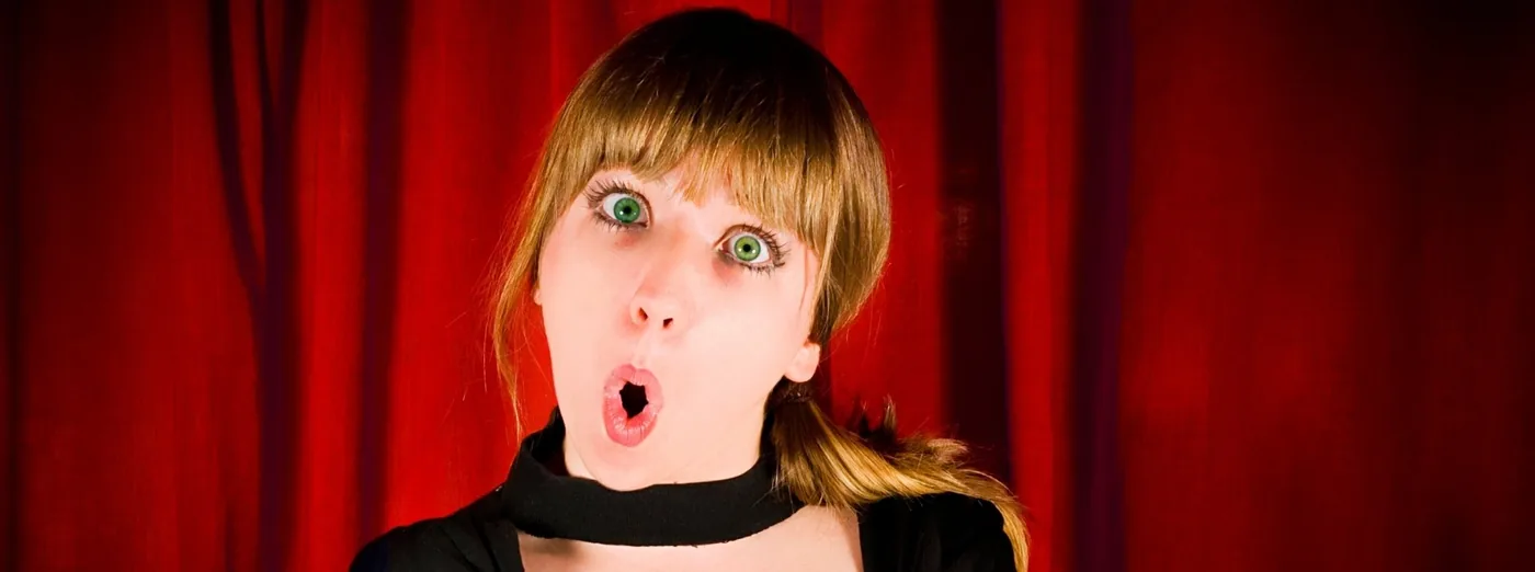Comédienne débutante à l'expression surprise devant un rideau rouge, cours de théâtre adultes à Nantes — L'École du Rire